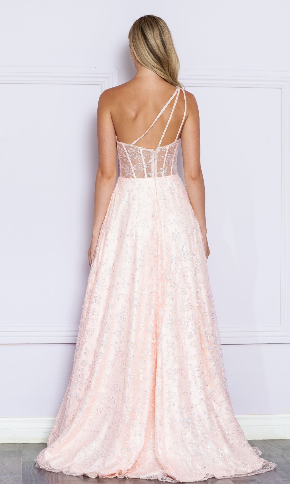A woman faces away wearing the One-Shoulder Embroidered Long Prom Dress 9372 in light pink, featuring sequin details, a sheer back panel, and asymmetrical spaghetti straps.
